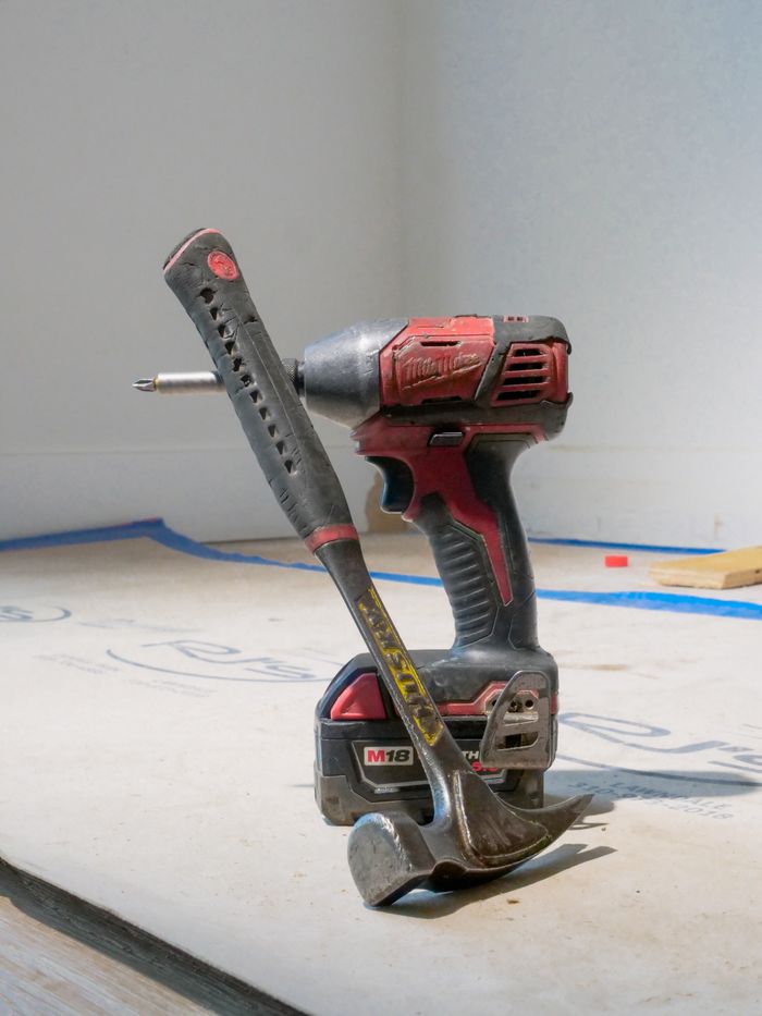 contact-img Close-up of a power drill and hammer on a construction site floor.
